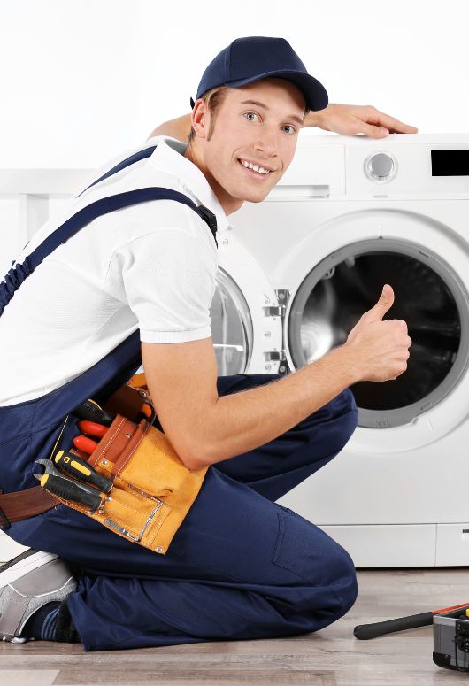 A man in overalls and work boots holds a thumbs up next to a washing machine, representing appliance repair services in Tampa, FL.