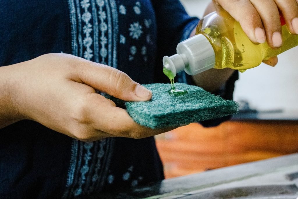 An individual is using a sponge to thoroughly clean a sink, focusing on removing stains and residue.