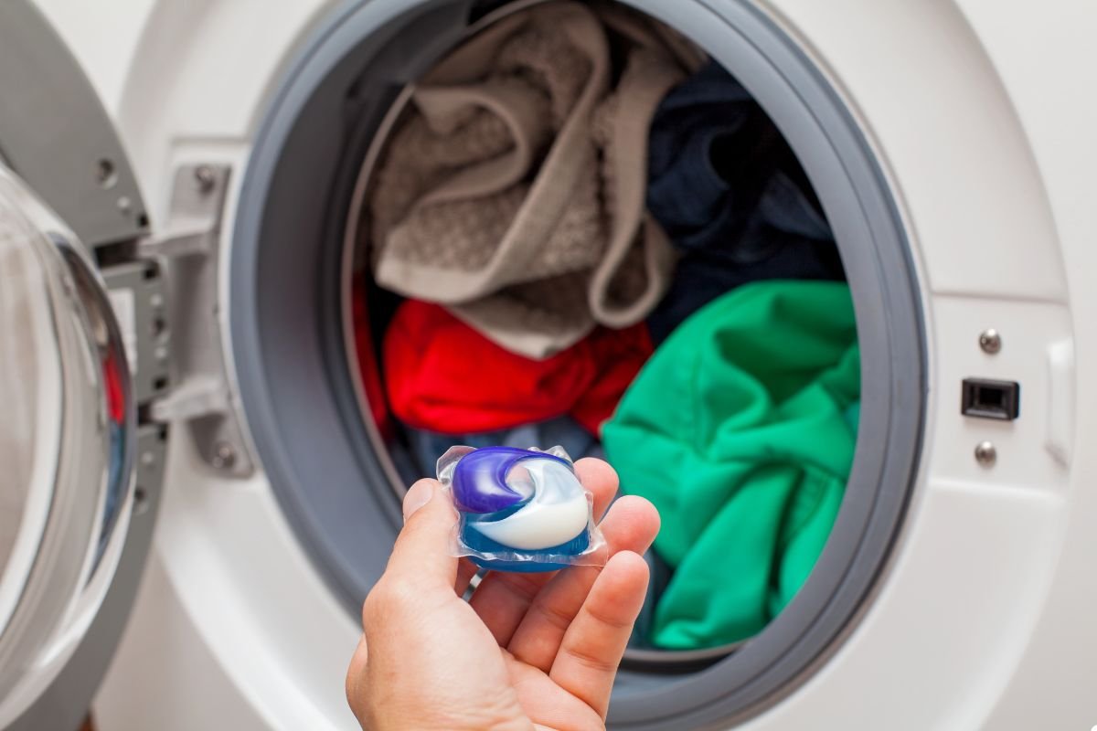 Individual holding a small ball in front of a washing machine, preparing for laundry or a related activity. 